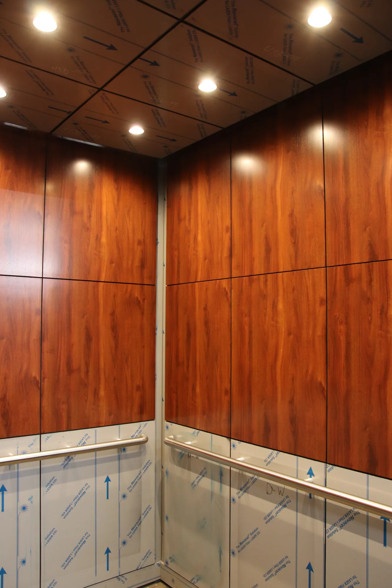 Warm wood veneer elevator cab at 226 Main Street with stainless handrails and recessed lighting